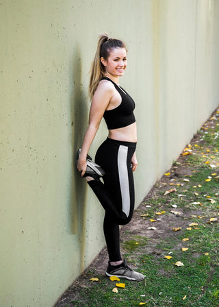Stylish Athleisure Outfit - Young woman wearing black and white athletic leggings and sports bra posing against a concrete wall.