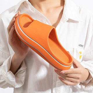 Vibrant orange flip flops with stripes, held in a person's hands against a white background.