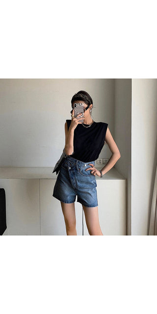 Classic black sleeveless straight shirt T-shirt with trendy denim shorts worn by a fashionable woman in a minimalist interior setting.