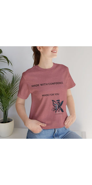 Trendy pink graphic t-shirt with inspirational text and butterfly design, showcased on a model in a casual setting with potted plants in the background.