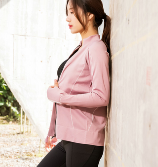 Stylish slim-fit pink sportswear, featuring a tailored design and long sleeves, worn by a young woman standing near a white wall.