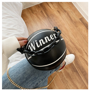 Black and white basketball-shaped leather satchel with "Winner" text, held in hand on hardwood floor