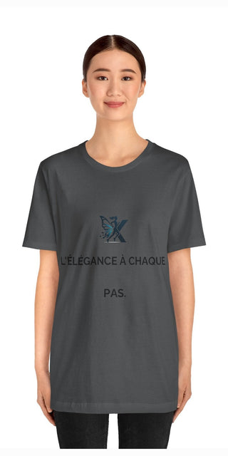 Stylish grey unisex t-shirt with printed butterfly logo and French text, modeled by a smiling young woman against a plain white background.