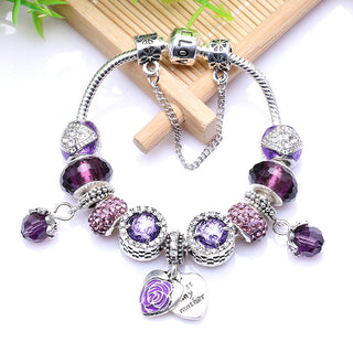 Elegant purple and silver charm bracelet with floral and crystal accents, displayed on a wooden background with green leaves.