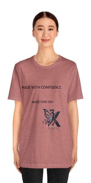 Stylish pink t-shirt with bold text "MADE WITH CONFIDENCE. MADE FOR YOU" and the K-AROLE logo. The model is wearing the trendy, comfortable unisex jersey short sleeve tee against a plain white background.