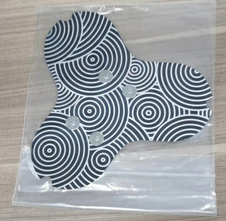 Patterned neck massager tool in plastic packaging, featuring a circular and swirling black and white design to help relieve tension.