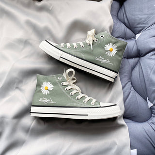 Trendy green high-top canvas sneakers with daisy flower print, showcased on a bedding background.