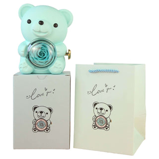 Mint-colored bear plush with a rose decoration, sitting on a gray gift box with a printed "I love you" message, along with a white paper gift bag with a similar bear print and text.