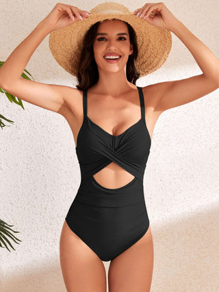 Stylish black one-piece swimsuit with cutout and waist tie, modeled against a bright, tropical backdrop.