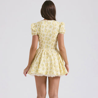 Yellow floral print dress with puff sleeves and v-neck design, worn by young woman with long dark hair.