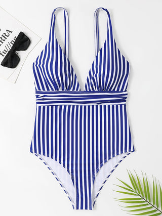 Blue and white striped one-piece swimsuit with a flattering silhouette, placed on a white background with a green palm leaf.