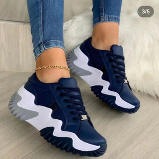 Navy blue and white lightweight breathable sneakers with wavy soles, featured on a female model's legs in a studio setting.