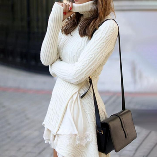 Cozy winter style: Elegant white cable-knit dress with long sleeves and a woman carrying a leather handbag.