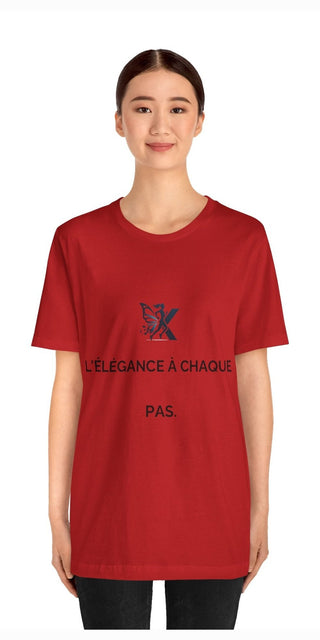 A woman smiling while wearing a bright red unisex jersey short sleeve t-shirt with a graphic design and text that reads "L'elegance a chaque pas" (French for "Elegance at every step").