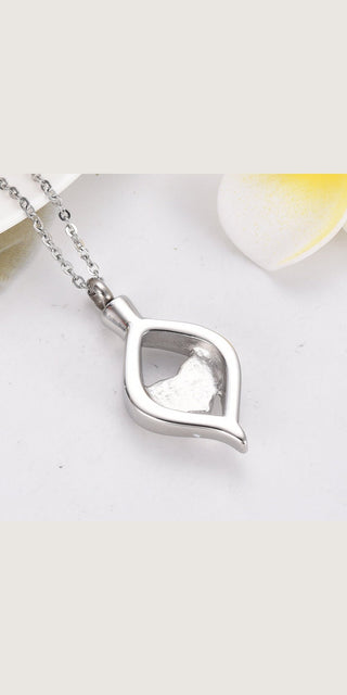 Elegant titanium steel heart-shaped ash box pendant on a silver chain, resting on a white surface with a soft light source.
