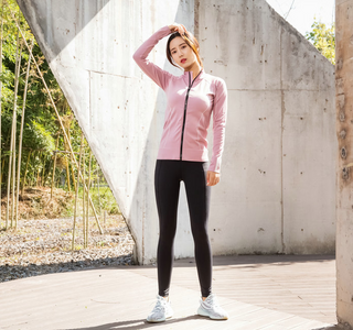 Slim fit sportswear - Stylish woman in pink zip-up jacket and black leggings poses in front of concrete wall.