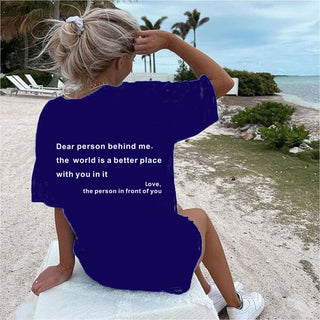 Woman on a beach with sandy shoreline and palm trees in the background wearing a navy blue T-shirt with a motivational message printed on it.