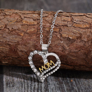 Elegant crystal heart-shaped pendant necklace with "Mom" text in gold on a wooden background
