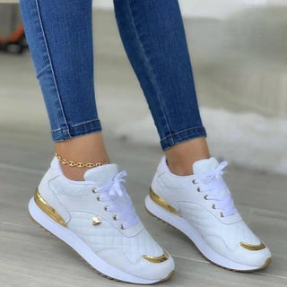 Stylish white and gold sneakers with lace-up closure and decorative details, worn with blue denim jeans on a gray background.