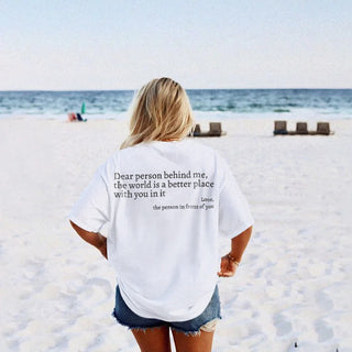Casual beach outfit with inspirational text printed on white t-shirt, woman standing on sandy beach with ocean view in the background