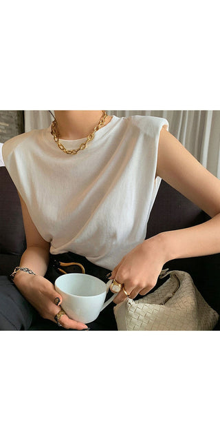 Sleeveless white blouse, gold chain necklace, woman's hands holding a coffee cup.
