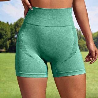 Mint green seamless high-waisted athletic shorts on a woman's body against a background of greenery and a clear sky.