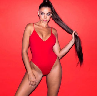 Striking red one-piece swimsuit with plunging neckline, showcasing model's long dark hair and alluring pose against vibrant red backdrop.