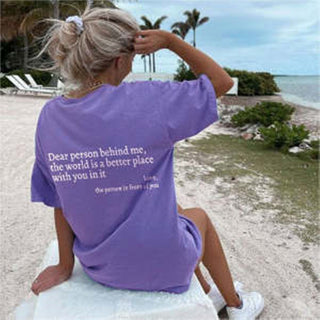 Fashionable women's t-shirt with positive message on the back, worn by a person enjoying the beach scenery.