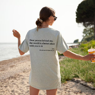 Stylish woman's T-shirt with inspirational message, "Dear person behind me, the world is a better place with you in it." Casual beachwear look captured in scenic outdoor setting.