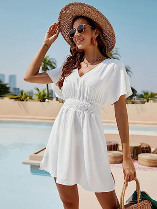 Elegant white cotton sundress with puffy sleeves, straw hat, and sunglasses worn by smiling woman by a pool.