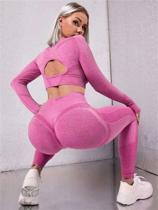 Vibrant pink seamless workout set: long sleeve crop top with cutout back and high-waisted leggings with contoured silhouette, worn with white sneakers.