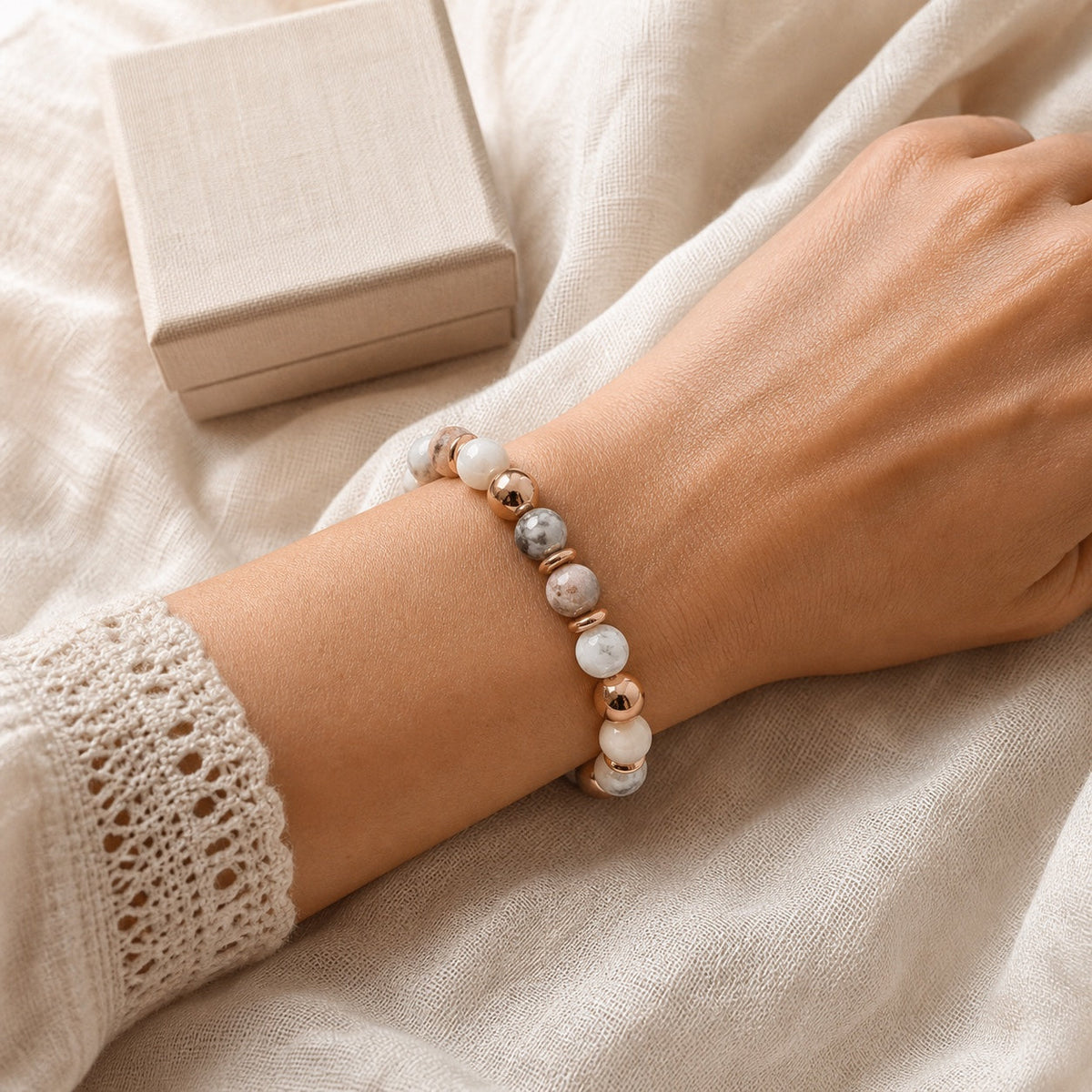 Bracelet en pierres naturelles rose, crème et grises avec détails rose doré porté au poignet