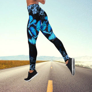 Vibrant blue butterfly print yoga pants on a person's legs standing on a paved road in a natural landscape.