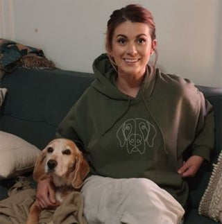 Smiling woman wearing cozy green hoodie, sitting with adorable dog on couch