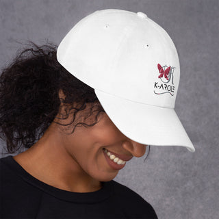 White K-AROLE dad hat with butterfly logo worn by a smiling person against a gray background