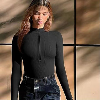 Sleek black long-sleeved jumpsuit with a high collar, worn by a young female model with long brunette hair, posing against a textured background.