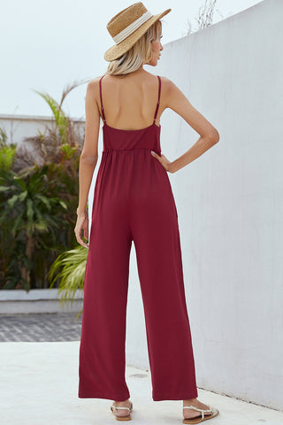 Chic burgundy linen jumpsuit with an open back, worn with a woven straw hat, showcased in a backyard setting with lush greenery.