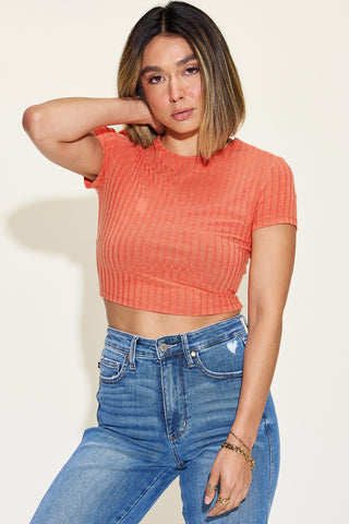 Stylish ribbed short sleeve crop top in vibrant orange color, worn with high-waisted blue denim jeans, showcased on a female model with long dark hair.