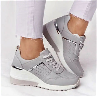 Stylish gray sneakers with perforated details and a wedge sole. The casual, sporty shoes feature a lace-up closure and a comfortable, cushioned design for daily wear. The sneakers are displayed against a plain background, allowing the fashionable footwear to take center stage.