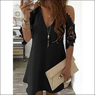 Elegant black lace-sleeved dress with gold necklace and clutch, styled for a fashionable look.