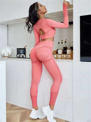 Stylish woman wearing seamless athletic set with long sleeve top and high-waisted leggings in a vibrant coral color, posing confidently in a modern kitchen setting.
