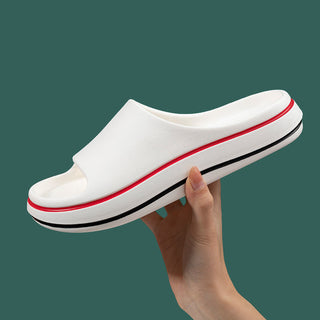 Comfortable white slip-on sandals with red and black accents, held in a hand against a dark green background.