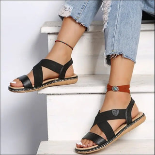 Black criss-cross strap flat sandals with a textured sole, worn with distressed denim jeans.