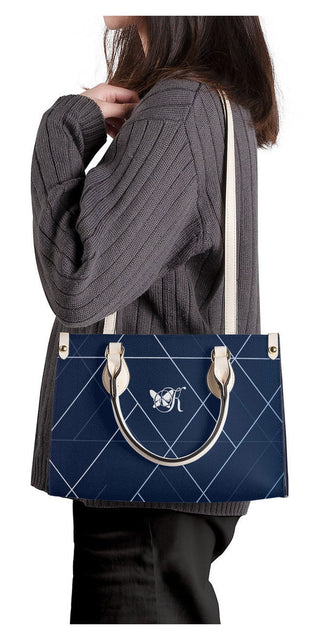 Stylish navy blue designer tote bag with brass-tone hardware, showcasing a classic quilted pattern that adds a touch of elegance. The bag is held by a woman wearing a gray sweater, highlighting the versatile and fashionable nature of this K-AROLE accessory.