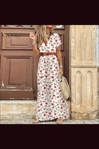 Elegant floral dress with flowing white skirt and red flower print, paired with a straw bag and worn by a woman standing in front of a wooden door.