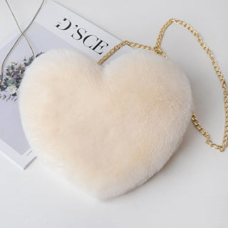 Stylish fluffy heart-shaped shoulder bag with a gold-tone chain strap, resting on a magazine against a plain background.