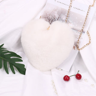 Soft, plush white shoulder bag with a chain strap, surrounded by a winter landscape, tropical leaves, and red cherries, creating a whimsical and stylish fashion accessory.