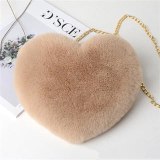 Plush heart-shaped shoulder bag in soft beige tone with a gold chain strap, resting on a fashion magazine.