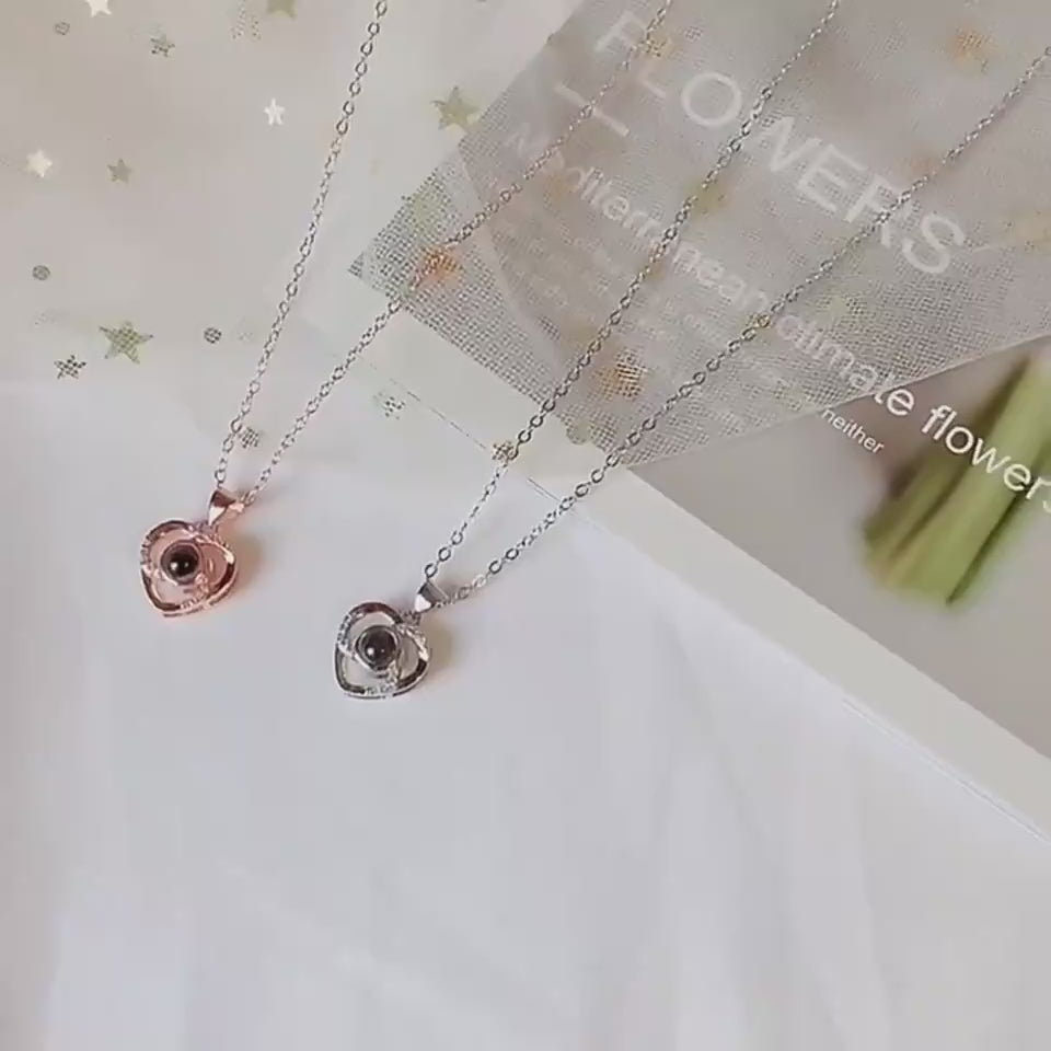 Elegant heart-shaped silver pendants on delicate necklace chains, suspended against a white and glitter-accented background, showcasing a romantic, feminine design.
