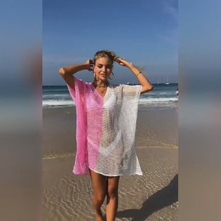 Fashionable pink and white knit beach cover-up dress on a sunny shoreline with sailboats in the background.